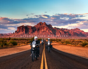 Welcome to Arizona: three motorcyclists ride a desert highway toward the Superstition Mountains at sunset.